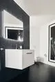 Moderne Badezimmeransicht mit einem hängenden weißen Waschbecken, einem großen Spiegel und einem Papierrollenhalter an der Wand. Ideal Standard Produkte sind in das Design integriert.
